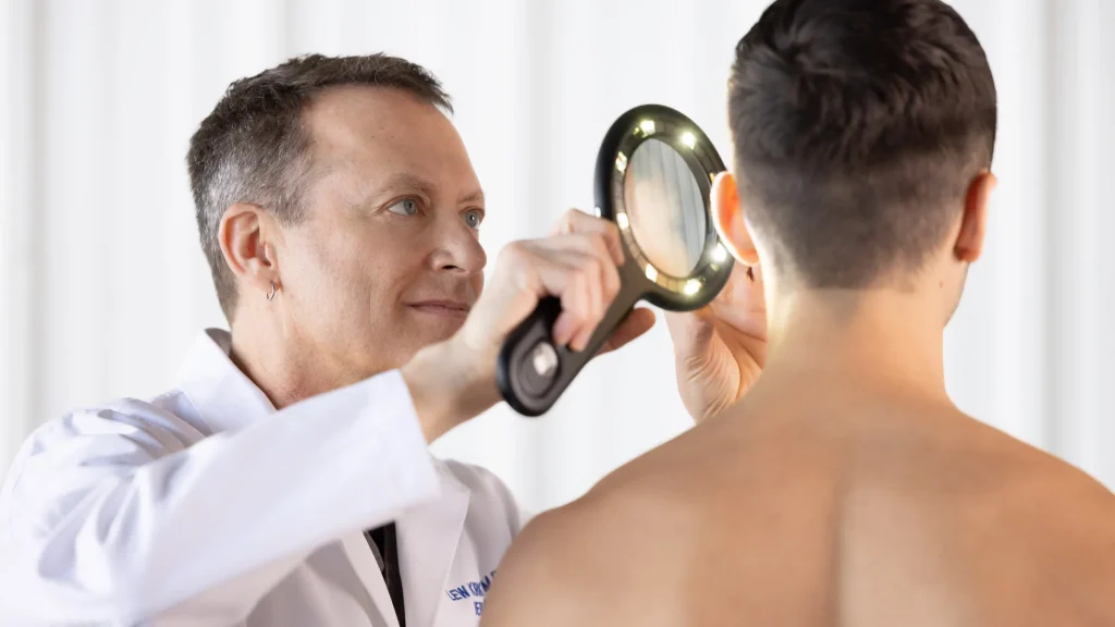 Dr. Kirkegaard examines the skin on a patient's ear with a lit magnifying glass