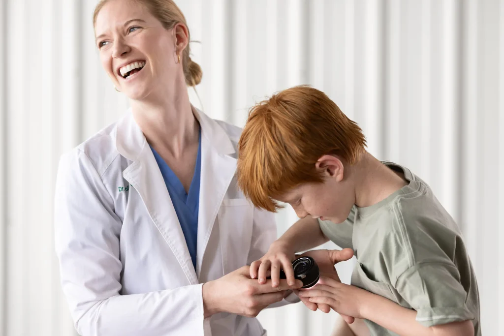 Dr Laggis, laughing, while working with a young patient who has taken control of the dermatoscope